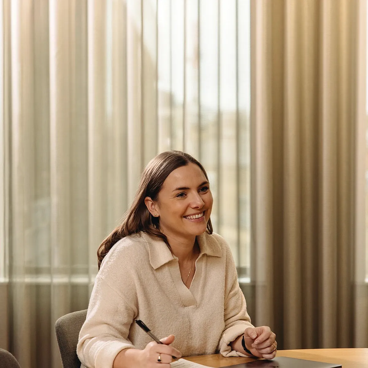 A smiling founder taking notes at a table in a warm, sunlit office