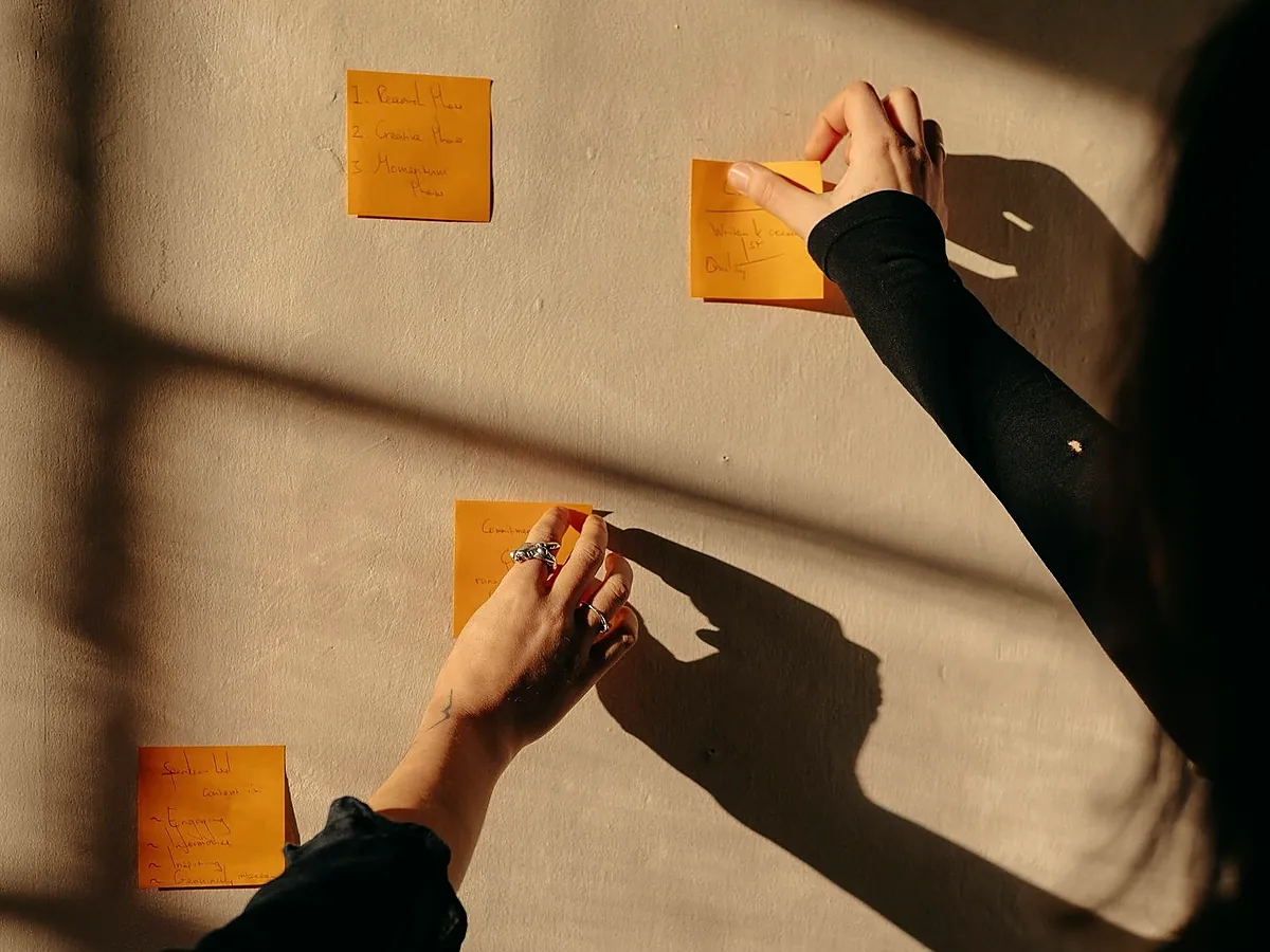 Hands placing sticky notes on a sunlit wall while mapping out a company