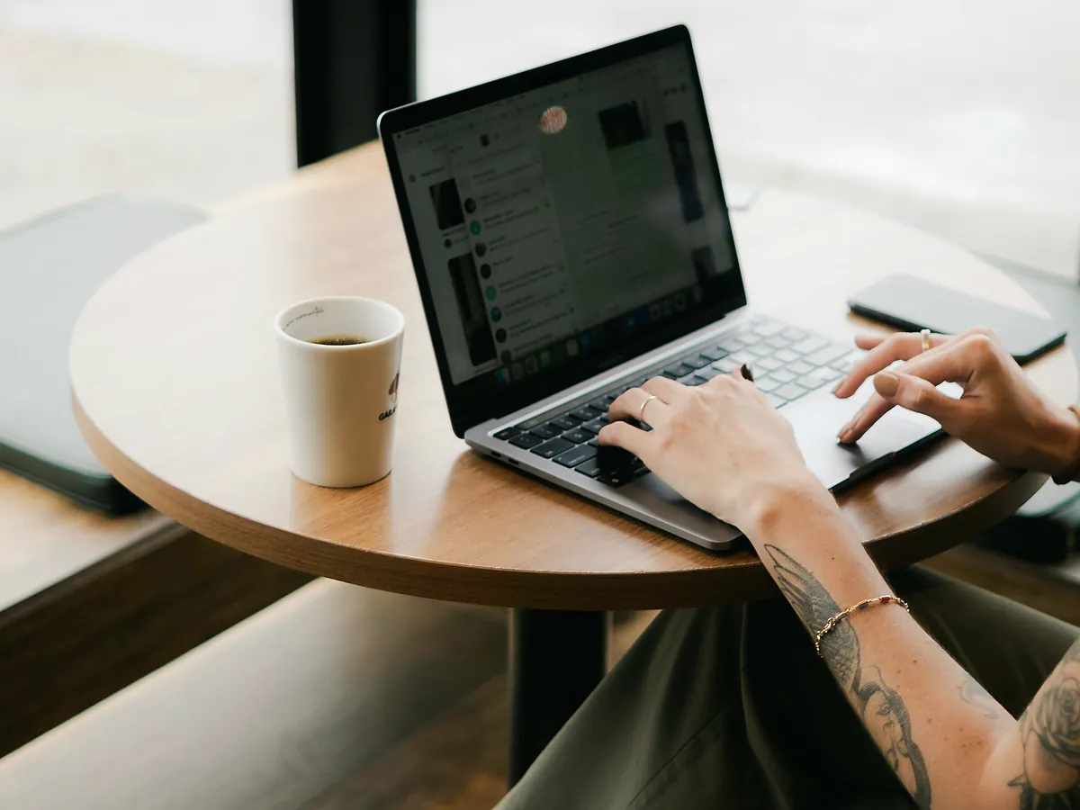 Hands typing on a laptop at a round table with a coffee