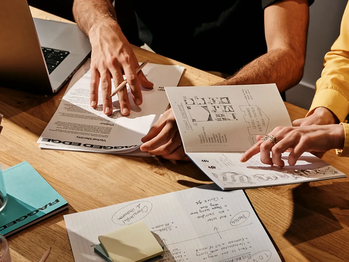 Hands going over printed plans and sketches on a wooden table